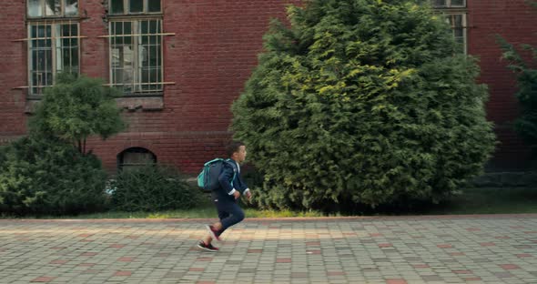 Side View of Little Boy in Uniform with Backpack Running Into Father hugs.Happy Young Man in Suit alt