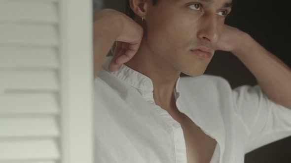 Attractive young man dresses a stylish white cotton shirt at home. Slow motion alt