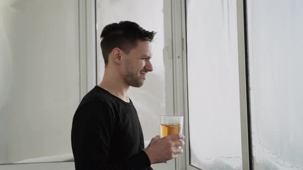 Caucasian Man with Cup of Tea Goes Out To Glazed Frozen Balcony on Sunny Day alt