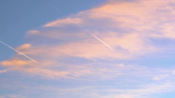Time lapse of two planes flying in parallel through orange clouds in a blue sky during sunset, inspi alt