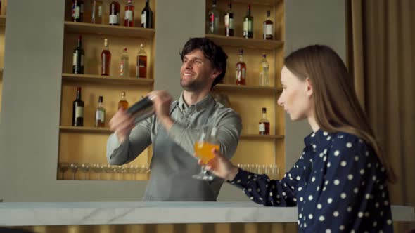 Man Bartender Working Preparing Cocktails at the Bar Talking to His Woman Client alt