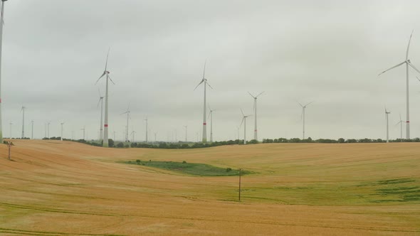 Forwards Fly Above Grain Field Surrounded By Wind Power Stations alt