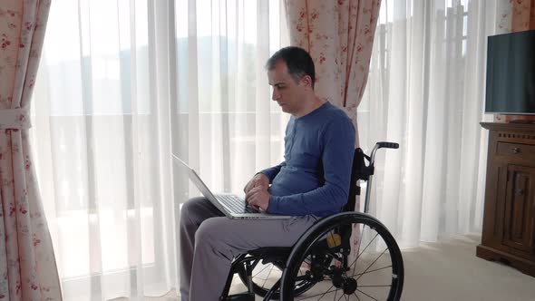 Young Man in Wheelchair Working at Laptop Computer at Home