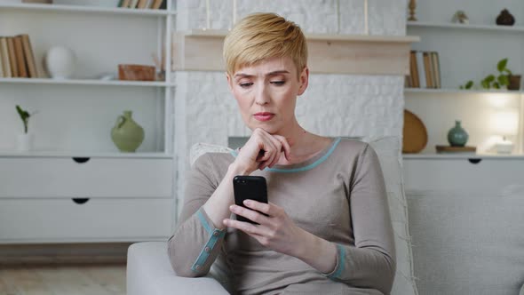 Frustrated Depressed Young Woman Sitting on Couch Holding Smartphone in Hands Received Message with alt