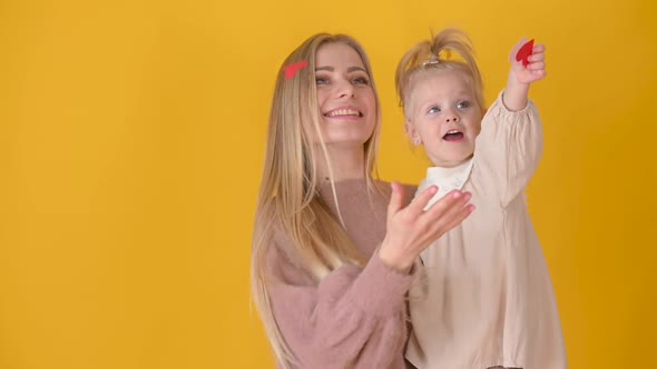 Happy young Mommy holds cute little daughter throwing holiday confetti alt