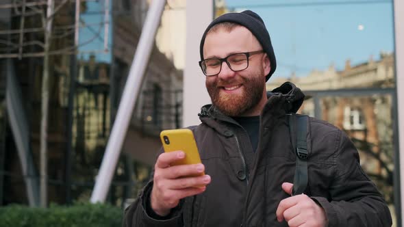 Handsome Bearded Man in 30s Looking at Phone Screen and Laughing While Walking at Street. Cheerful alt