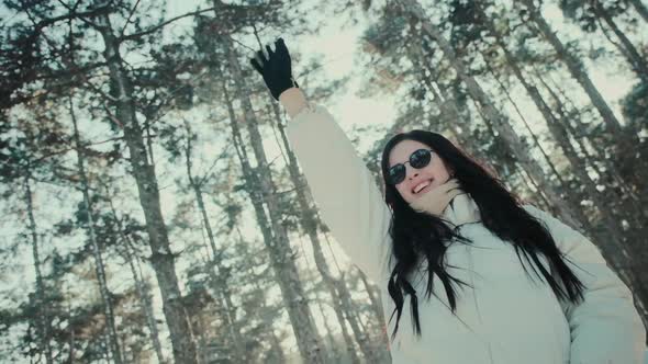 Happy Woman with Sunglasses Waves Hand in Winter Forest