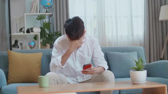 Asian Man Being Tired While Using Smartphone In The Living Room alt