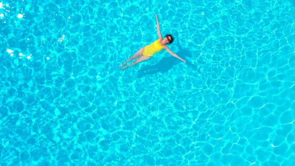 View From the Top As a Woman in a Yellow Swimsuit Lying on Her Back in the Pool alt