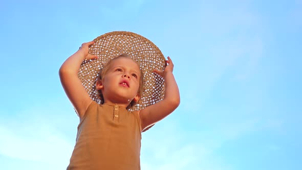 Adorable Smiling Boy in Straw Hat on Blue Sky Background alt