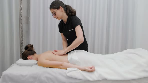 Female therapist massages a young woman on her back and shoulders. Relaxing massage.