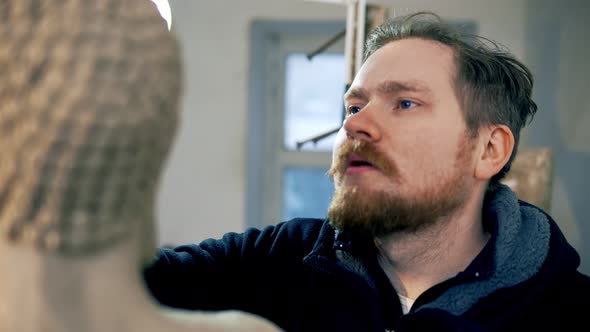 Concentrated Artist Working on Buddha Statue Face Using a Special Tool at Workshop alt