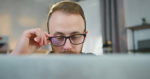 Man in Glasses which Sitting at his Workplace in front of Laptop  alt