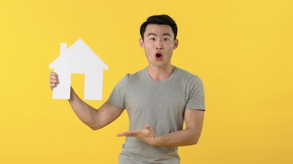 Young Asian man in gray t-shirt looking at and pointing to house cutout model