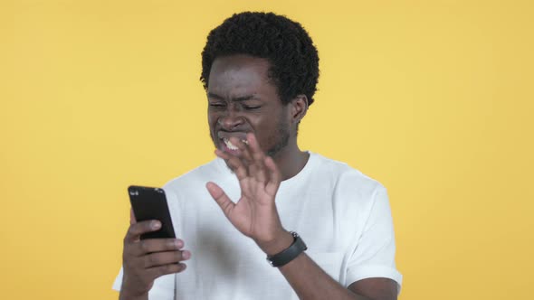 African Man Reacting To Loss on Smartphone, Yellow Background alt