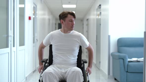 Man Rolling Wheelchair Along Hospital Corridor Looking Around alt