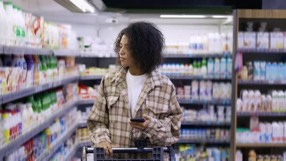 African American Lady Checking Grocery List on Smartphone at Supermarket alt