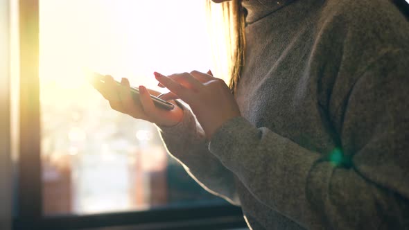 Female Hands Using Smartphone Against a Blurred Cityscape in the Setting Sun alt