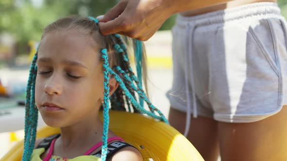 A Girl in a Suit Weaves African Braids in Her Hair on a Sunny Day alt