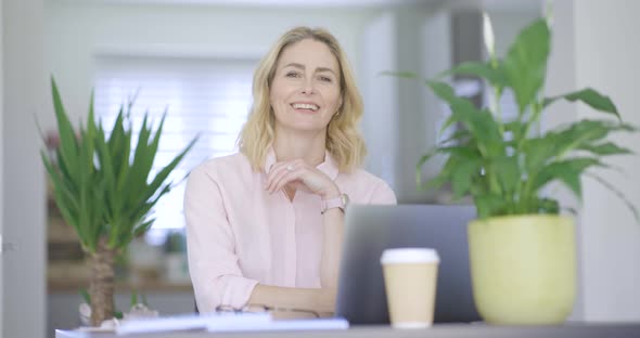 Smiling businesswoman sitting at desk with arms crossed