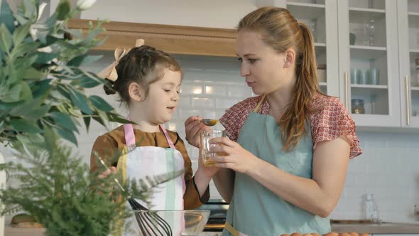 Woman Feeds Little Girl with Raw Yolk Making Pie in Kitchen alt