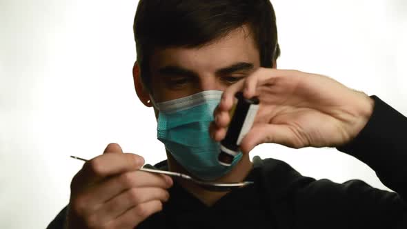 Portrait of a Young Man in a Medical Mask Makes Dripping Drops of Medicine Into a Spoon Removes the alt