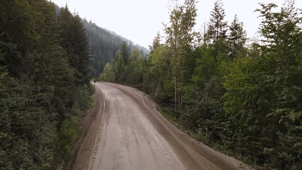 Silver car driving into a vast boreal forest in British Columbia that is covered with smoke from wil alt