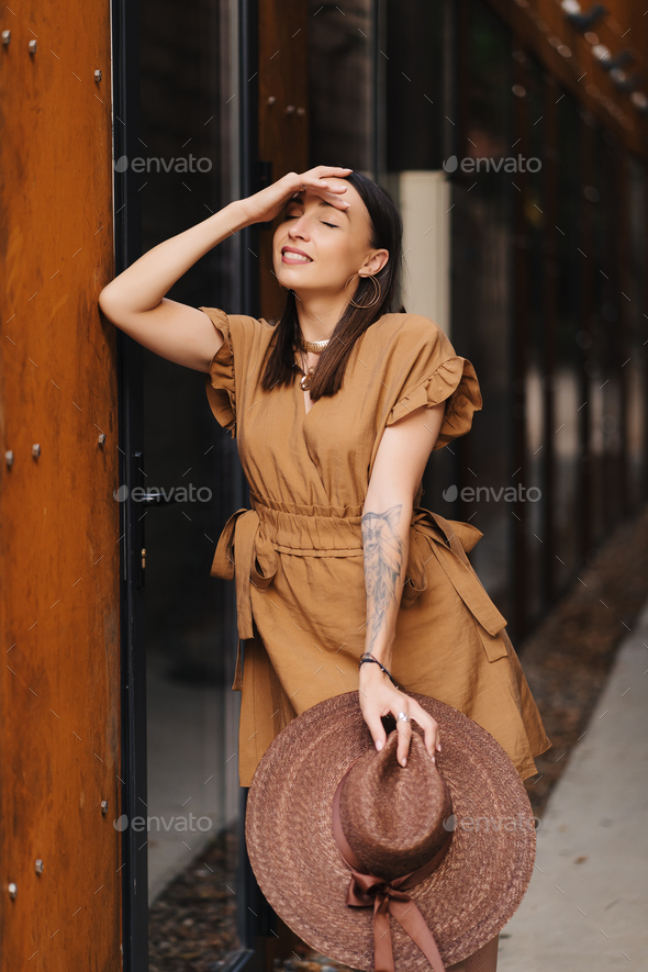 Young fashion girl dressed in a summer dress with a wicker wide hat walks  and poses in the old city Stock Photo by diignat