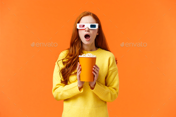 Shocked and tensed redhead woman seeing intense fight on screen as watching movie at cinema, wear 3d