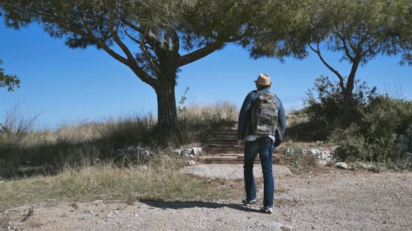Tourist with a Backpack Walks Along a Trail to a Hill Camera Tracking alt