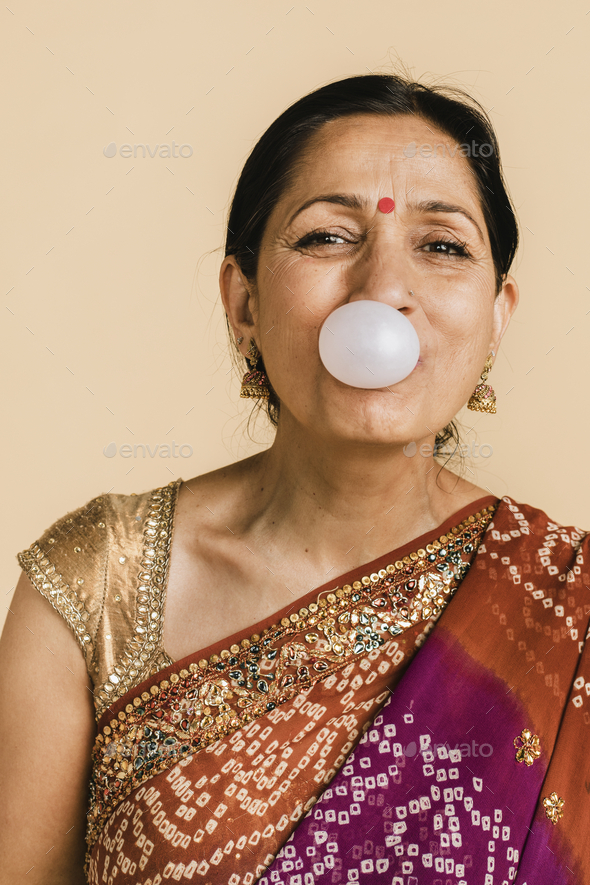 Senior Indian woman in a traditional saree blowing a bubble with a