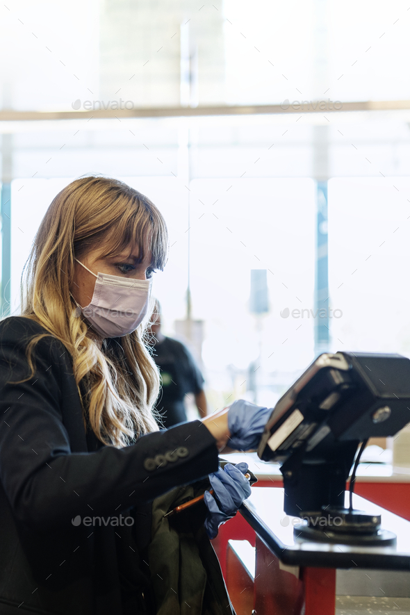 Woman in face mask wearing gloves while purchasing at self-checkout during coronavirus quarantine