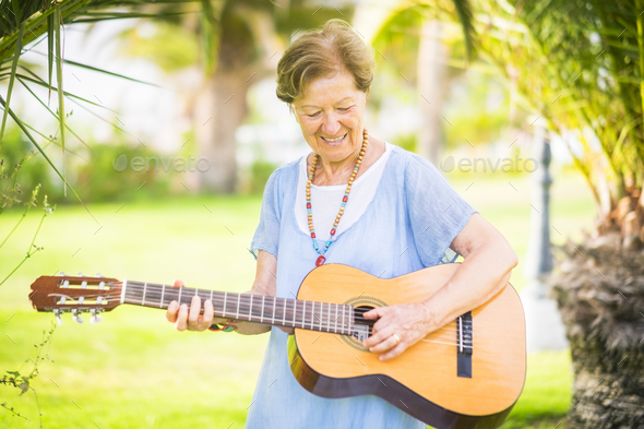 Cheerful and happy old aged senior caucasian woman smiling and having fun playing a guitar