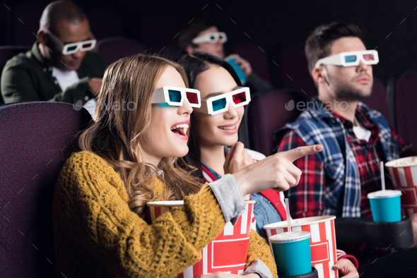 young smiling friends in 3d glasses with popcorn watching film in movie theater