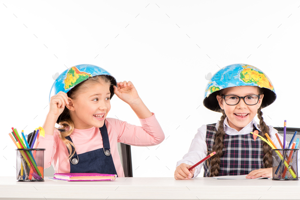 Happy schoolgirls sitting with halves of globe on heads isolated on white