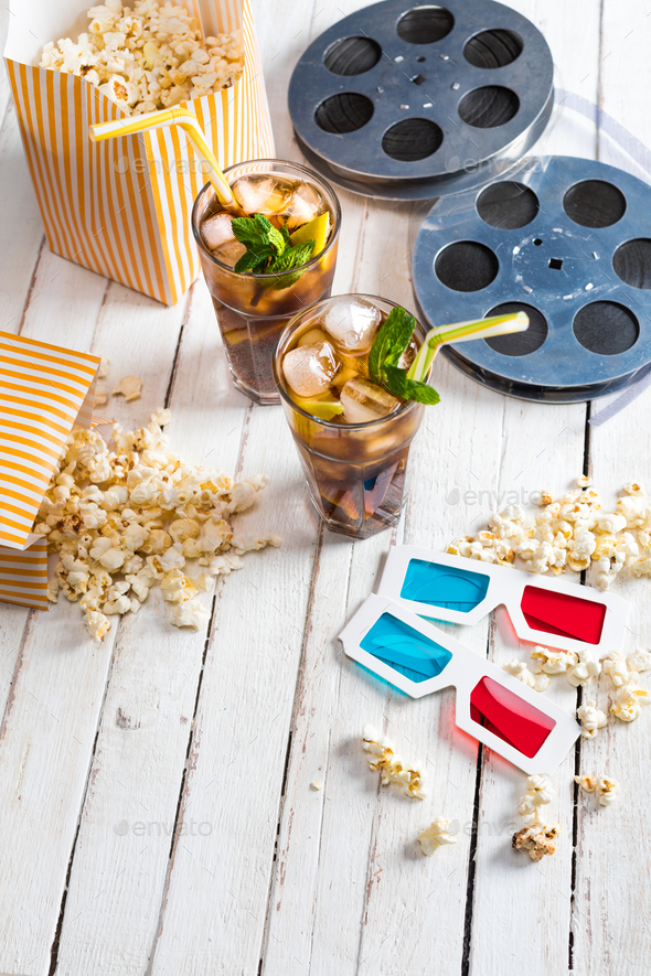 Close-up view of popcorn with iced tea, film reels and 3D glasses on table, Movie time concept
