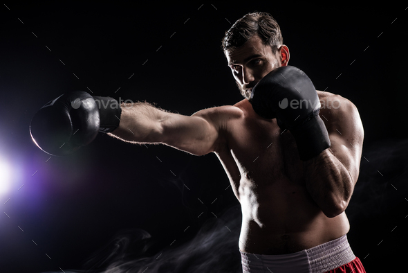 Young professional boxer in gloves punching the air isolated on black