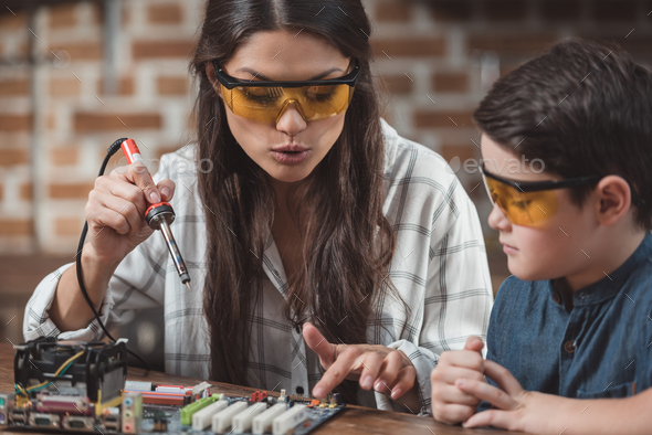 Little son and his beautiful mother working with soldering iron on electronics school project