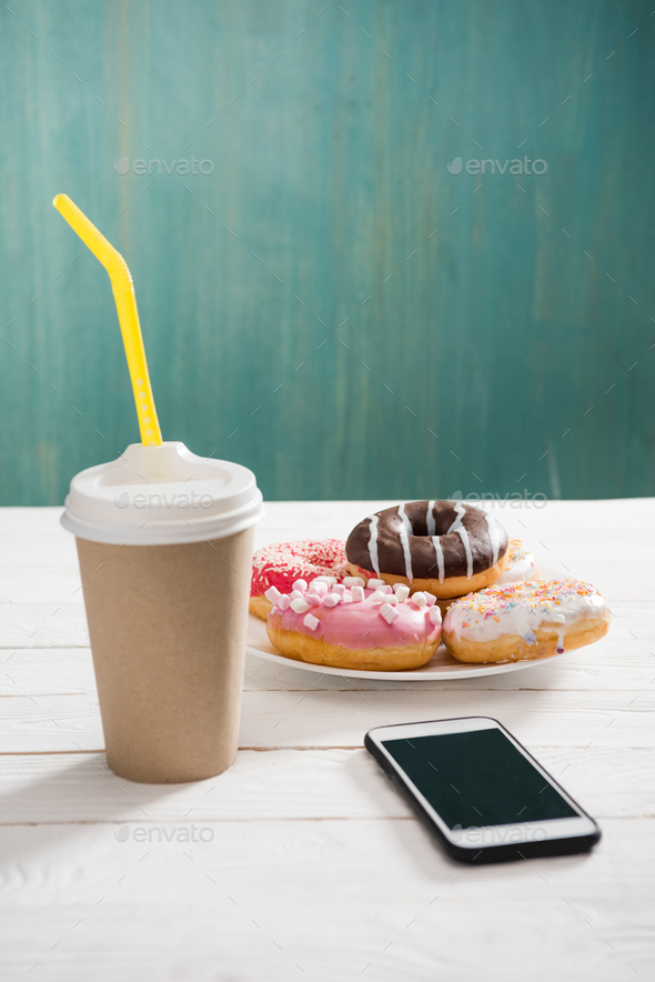 Unhealthy breakfast with coffee to go, plate of frosted donuts and smartphone wth black screen on