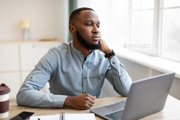 Bored Black Business Guy Sitting At Laptop At Workplace Indoors