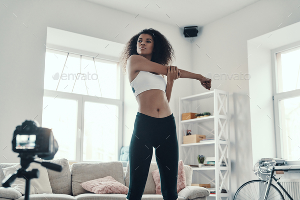 Beautiful young African woman stretching after hard work out while making social media video