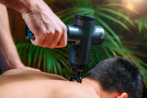 Therapist Treating Patient's Trapezius Muscle with Massage Gun Stock Photo  by microgen