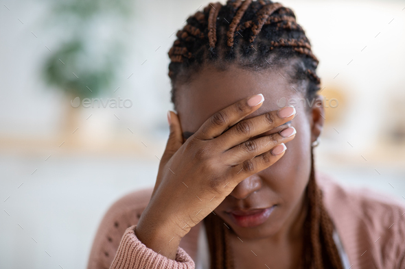Closeup portrait of depressed young black woman touching head in despair
