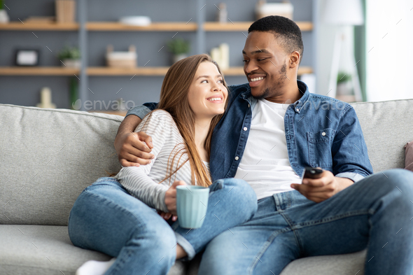 Happy Mixed Race Couple Relax On Couch In Living Room Watch Movie