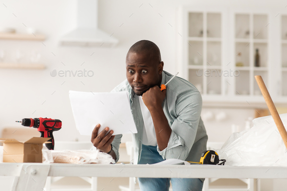 Problems with new furniture assembly. Shocked african american man reading instructions at home