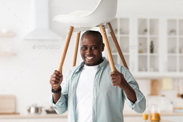 Furniture repair concept. Positive black man having fun with ready-made chair and raising it above