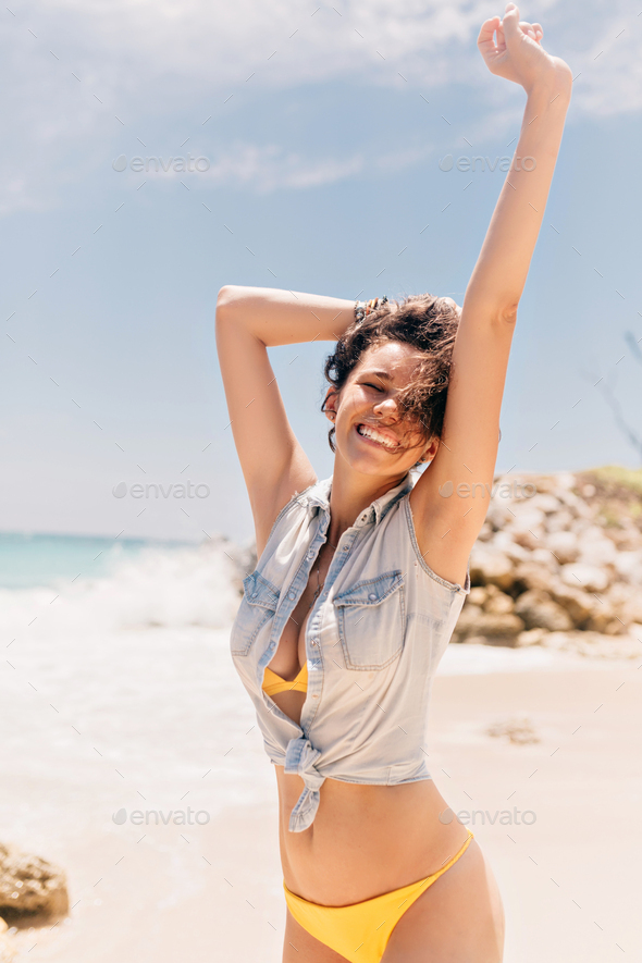 pretty charming lady in swim suit and denim jacket holding up hand on background of ocean
