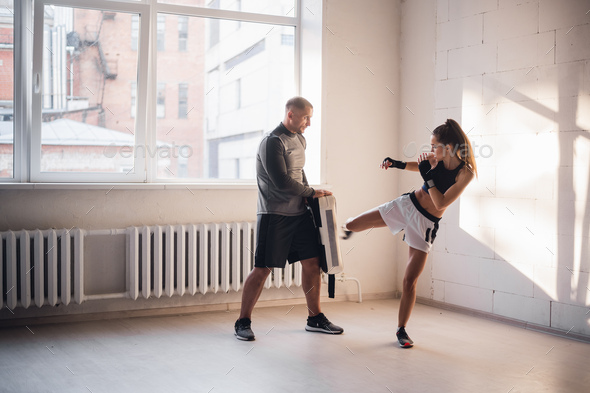 Female martial arts fighter practicing leg kick or high kick with her trainer in a boxing studio at