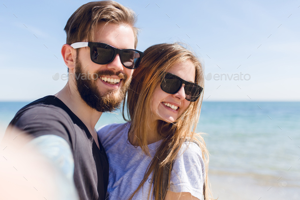 Close-up self-portrait of young couple standing near sea. She has long hair and smiling to the
