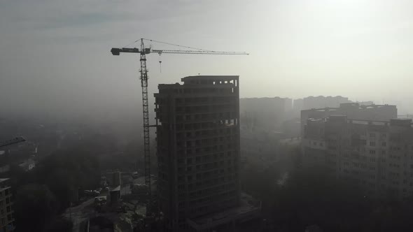Birds eye view on tower crane in fog standing next to residential building. 